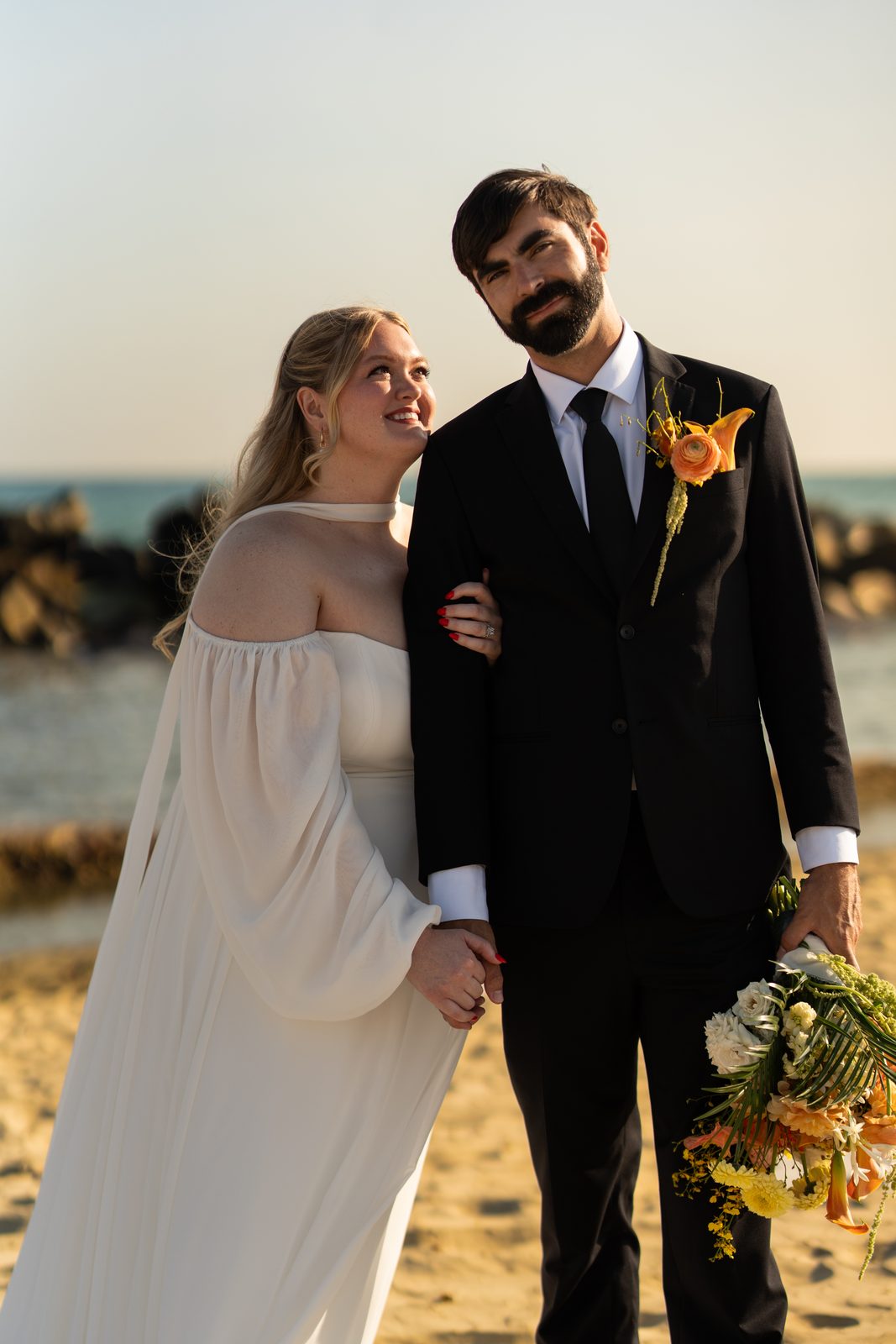 Bride leaning on the groom's shoulder by the ocean at golden hour