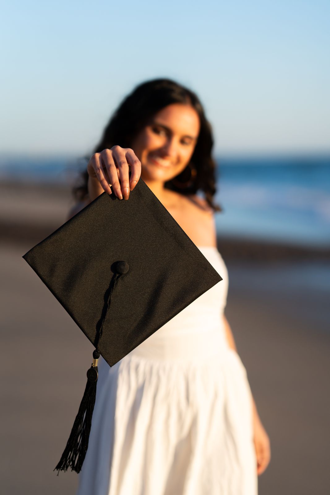 Graduate holding her cap toward the camera at the beach