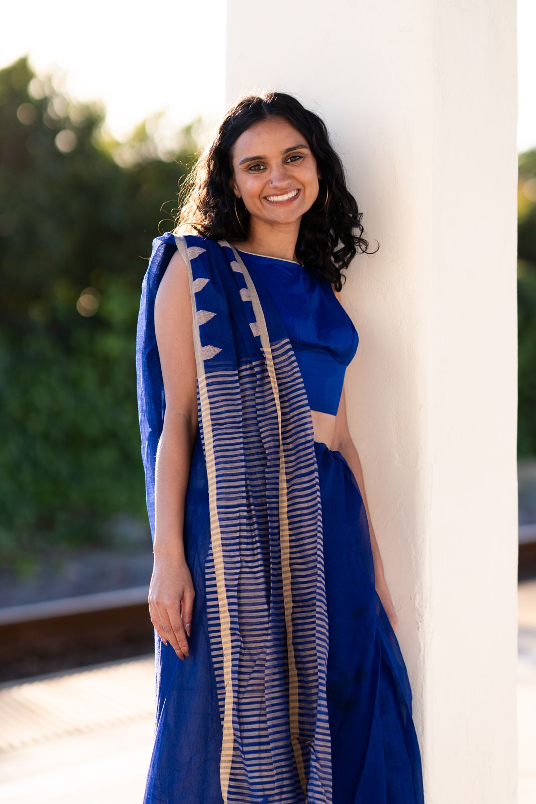 Woman in a royal blue saree smiling against a white pillar