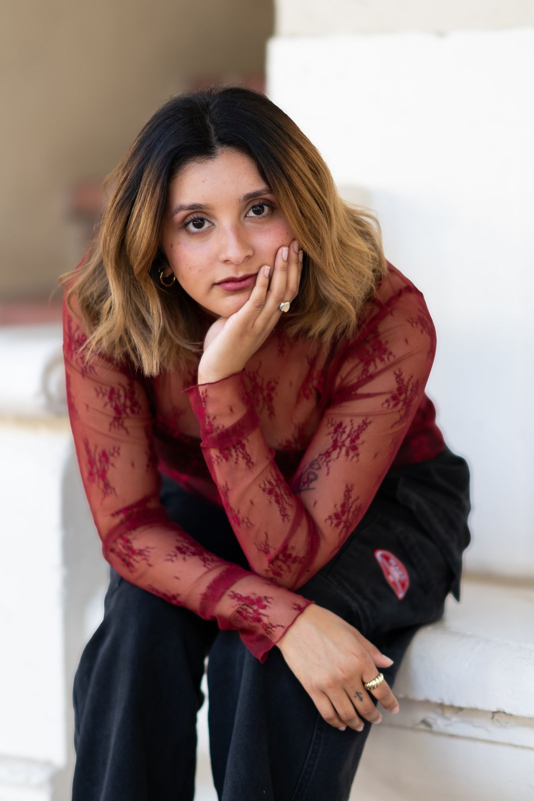 Woman in a red lace top resting her chin on her hand