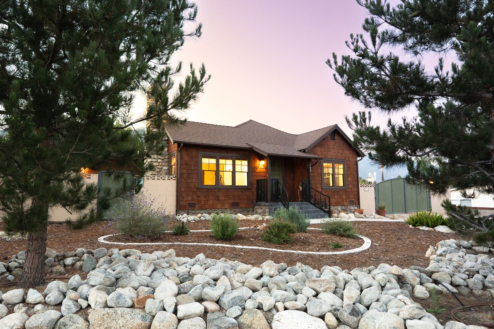 Cottage at dusk with glowing windows and a rock garden